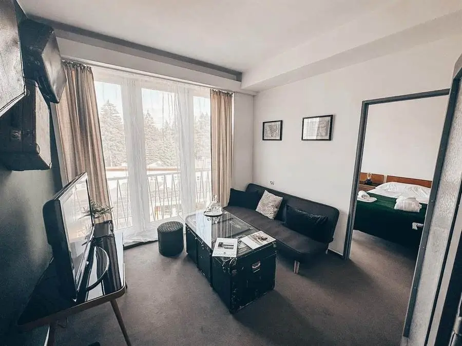 Obývací část apartmá se starožitným kufrem místo stolku, gramofonem a ložnicí v pozadí