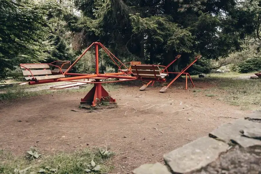 Původní červený retro kolotoč s dřevěnými lavičkami pod smrky v areálu hotelu